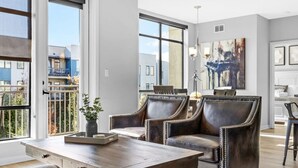 Ein geräumiges Wohnzimmer mit großem Fenster, einem Holztisch, Ledersesseln und einem Essbereich mit einer Chandelüster.