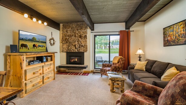 A cozy living room with a fireplace, wooden furniture, and a television displaying a countryside scene. - Pool, Hot Tub, Weber Gas BBQ, Renovated. Easy access into unit (Steamboat Springs)