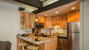 A modern kitchen with wooden cabinets, a granite countertop, stainless steel appliances, and a bar stool. - Pool, Hot Tub, Weber Gas BBQ, Renovated. Easy access into unit (Steamboat Springs)