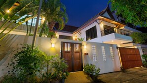 A modern house with a gated entrance, surrounded by lush greenery and potted plants.