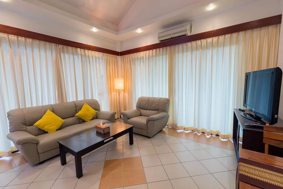 A living room with a beige sofa, two armchairs, a coffee table, a TV, and a lamp.