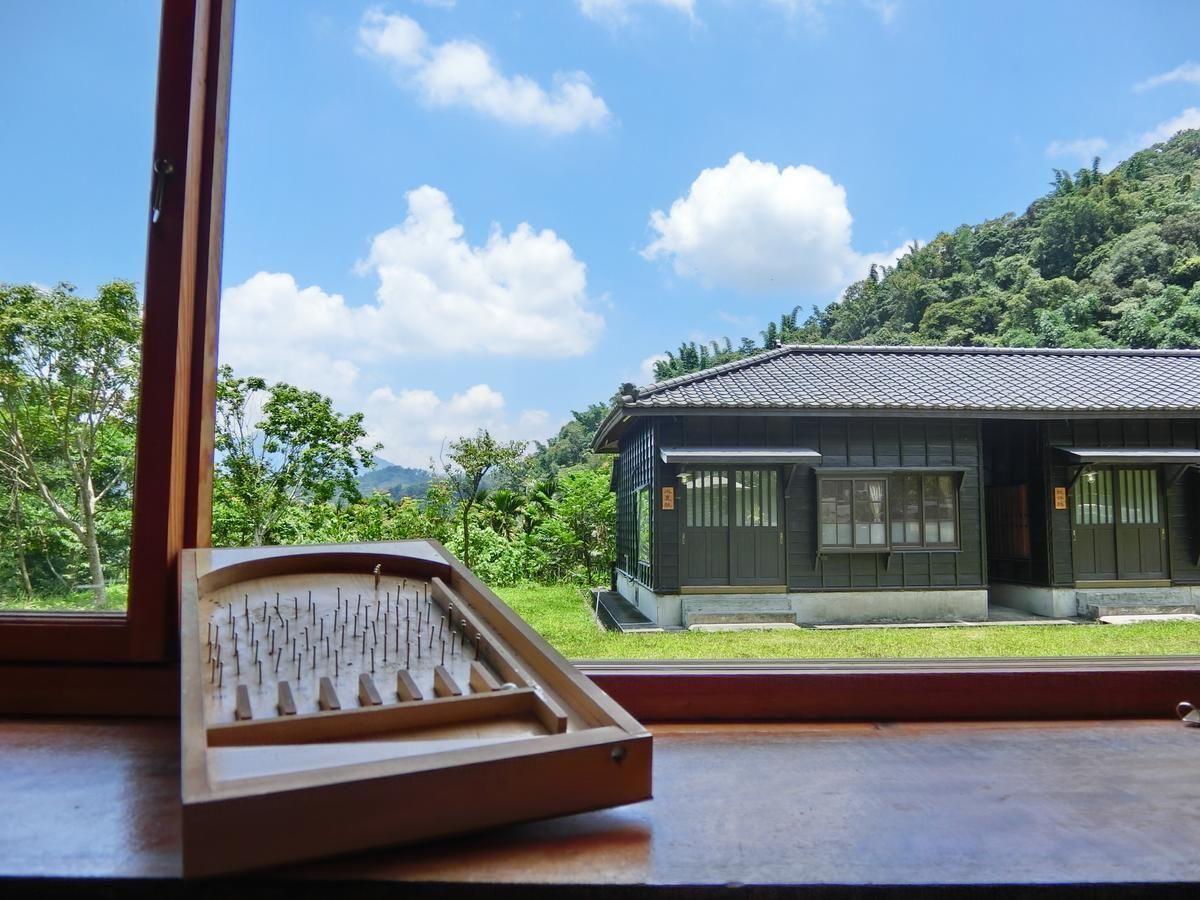 A traditional Japanese building with a tiled roof, surrounded by lush greenery and hills.