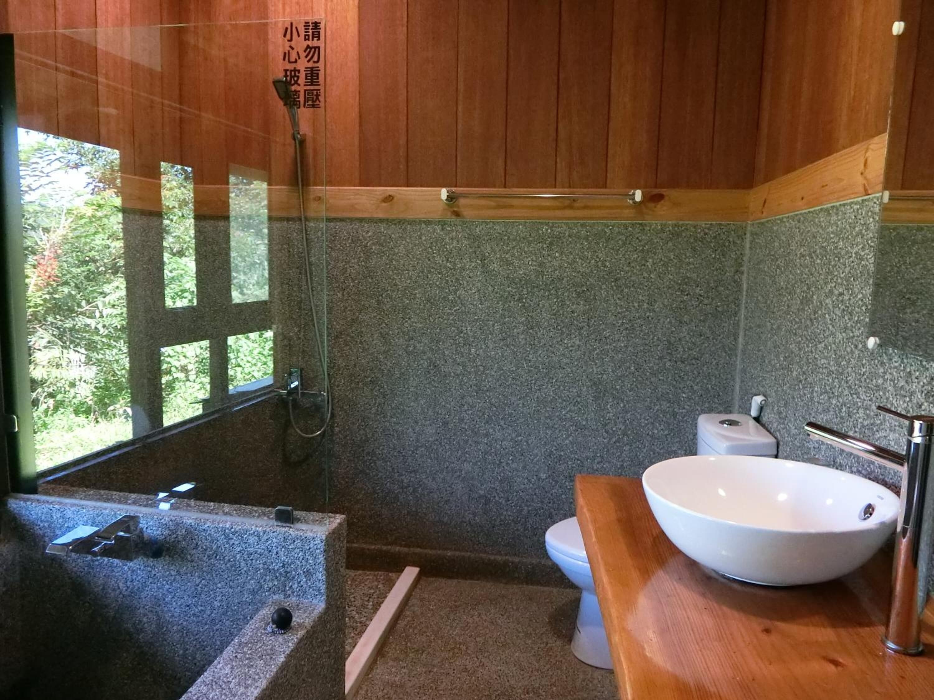 A bathroom with a wooden ceiling, a stone wall, a white sink, and a toilet.