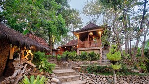 A rustic wooden house with a thatched roof, stone steps, and a garden with tropical plants. - RAJAKLANA Resort, Villa And Spa (Bangunjiwo)