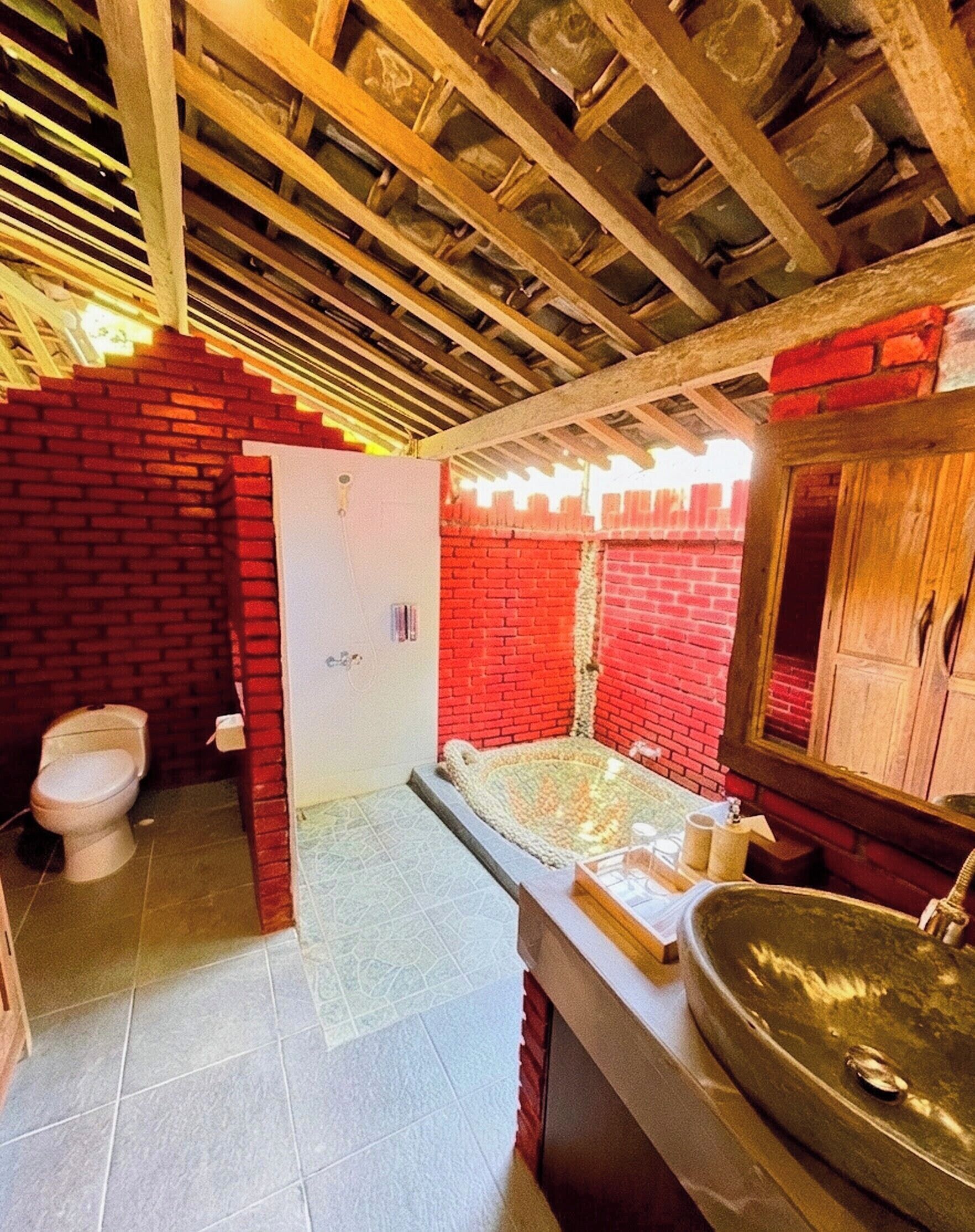 Ein Badezimmer mit roter Backsteinwand, einer weißen Toilette, einer Badewanne und einem Waschbecken.
