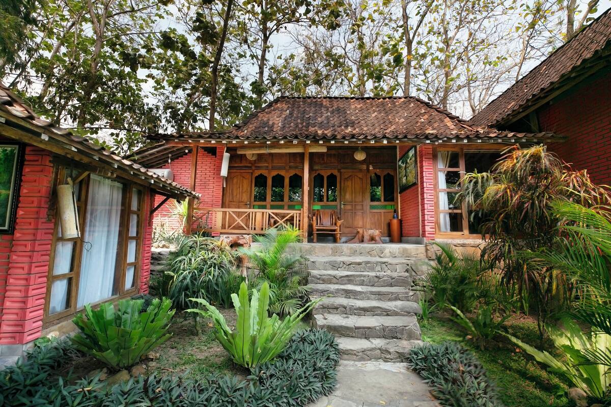A traditional house with a red brick exterior, wooden porch, and stone steps leading to a wooden door.
