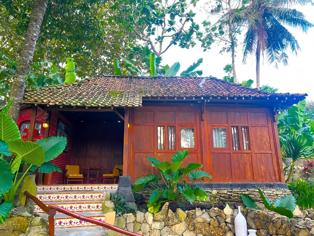 A rustic wooden building with a tiled roof, a porch with a stone base, and a staircase leading to the entrance.