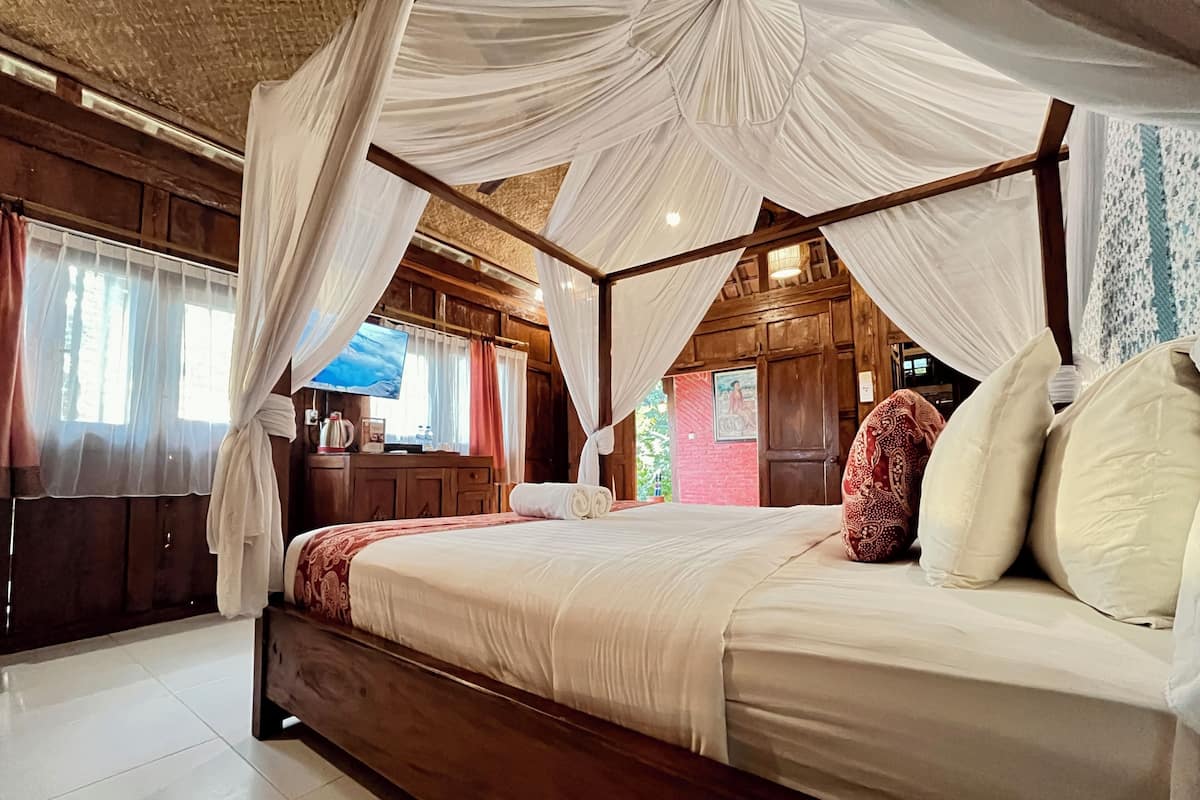 A four-poster bed with a canopy, wooden walls, a television, and a red brick wall in the background.