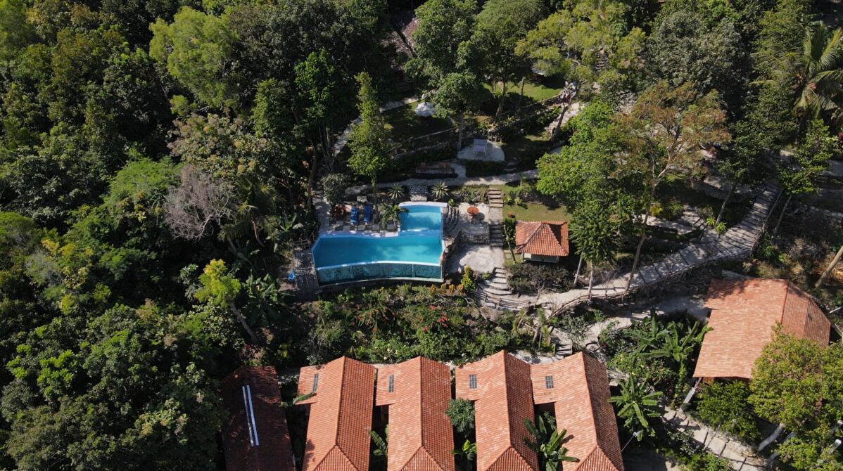 Luchtbeeld van een resort met een groot zwembad, omgeven door weelderige begroeiing, meerdere bungalows en een verzorgd landschap.