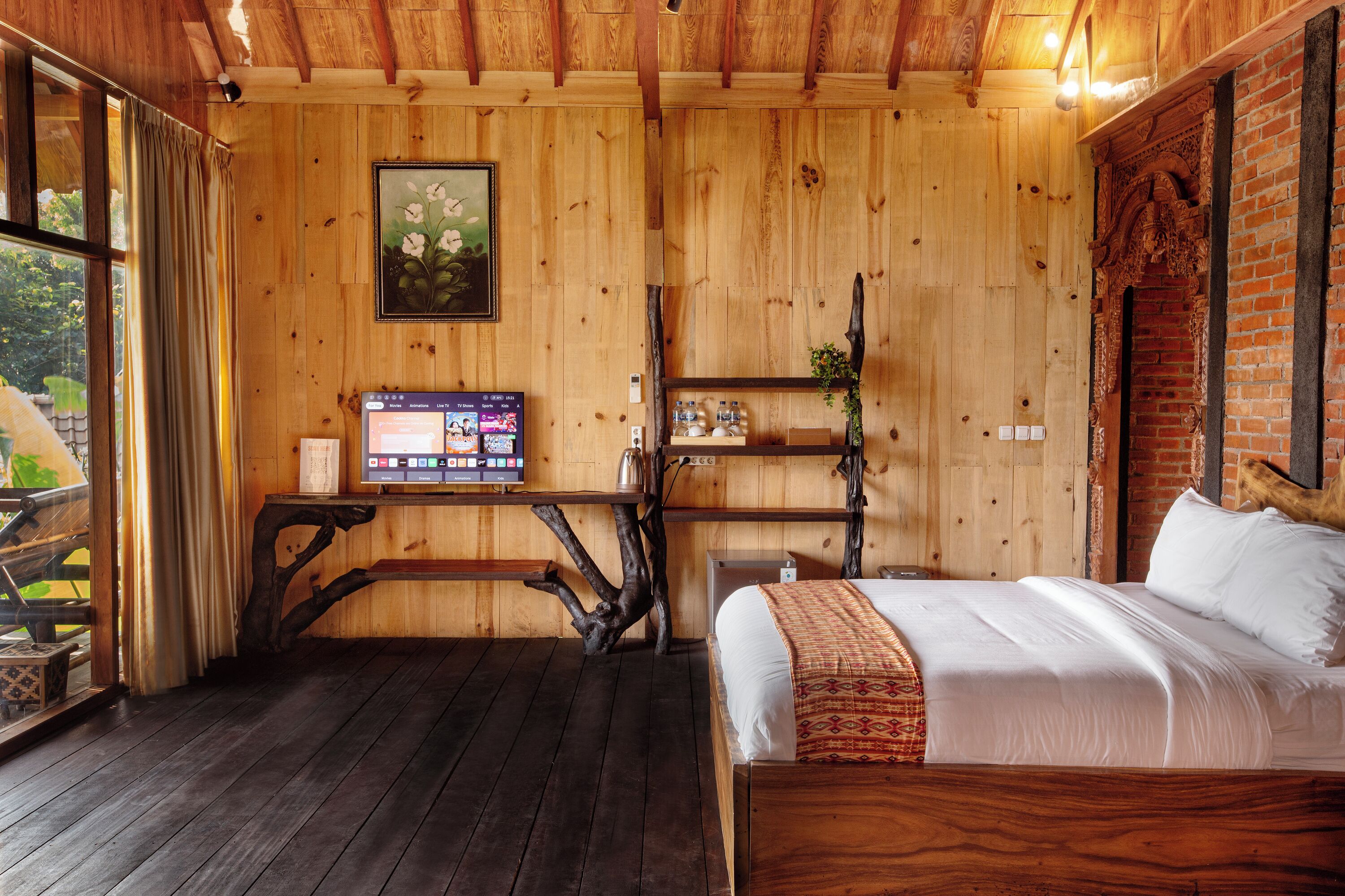 A wooden room with a bed, a desk with a computer, and a shelf with decorative items.