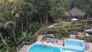 A swimming pool with lounge chairs and a stone wall. - RAJAKLANA Resort, Villa And Spa (Bangunjiwo)