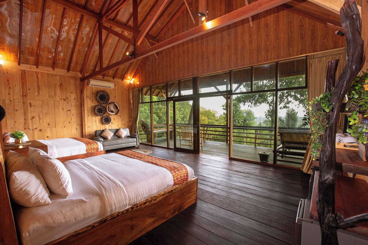 A spacious bedroom with a large bed, a sofa, and a balcony with a view of the outdoors.