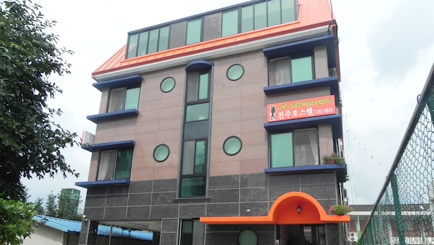 A multi-story hotel with a modern design, featuring a prominent orange awning and a sign indicating it is a guesthouse and hotel.