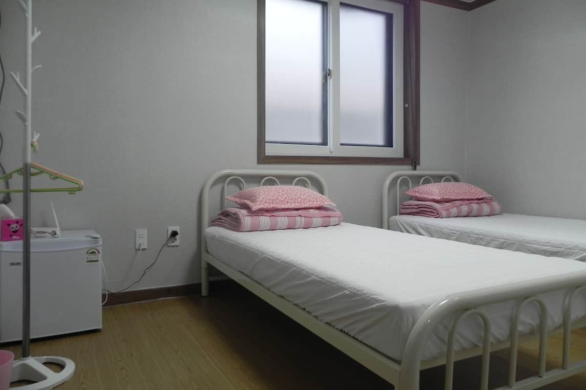 A bedroom with two single beds, a bedside table, a small heater, and a window.