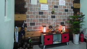 A room with a brick wall, a wooden shelf with various items, a clock, and a fire extinguisher.