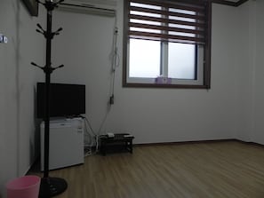 Una habitación con piso de madera, un televisor sobre un mueble bajo, una mesita y una ventana con persianas.