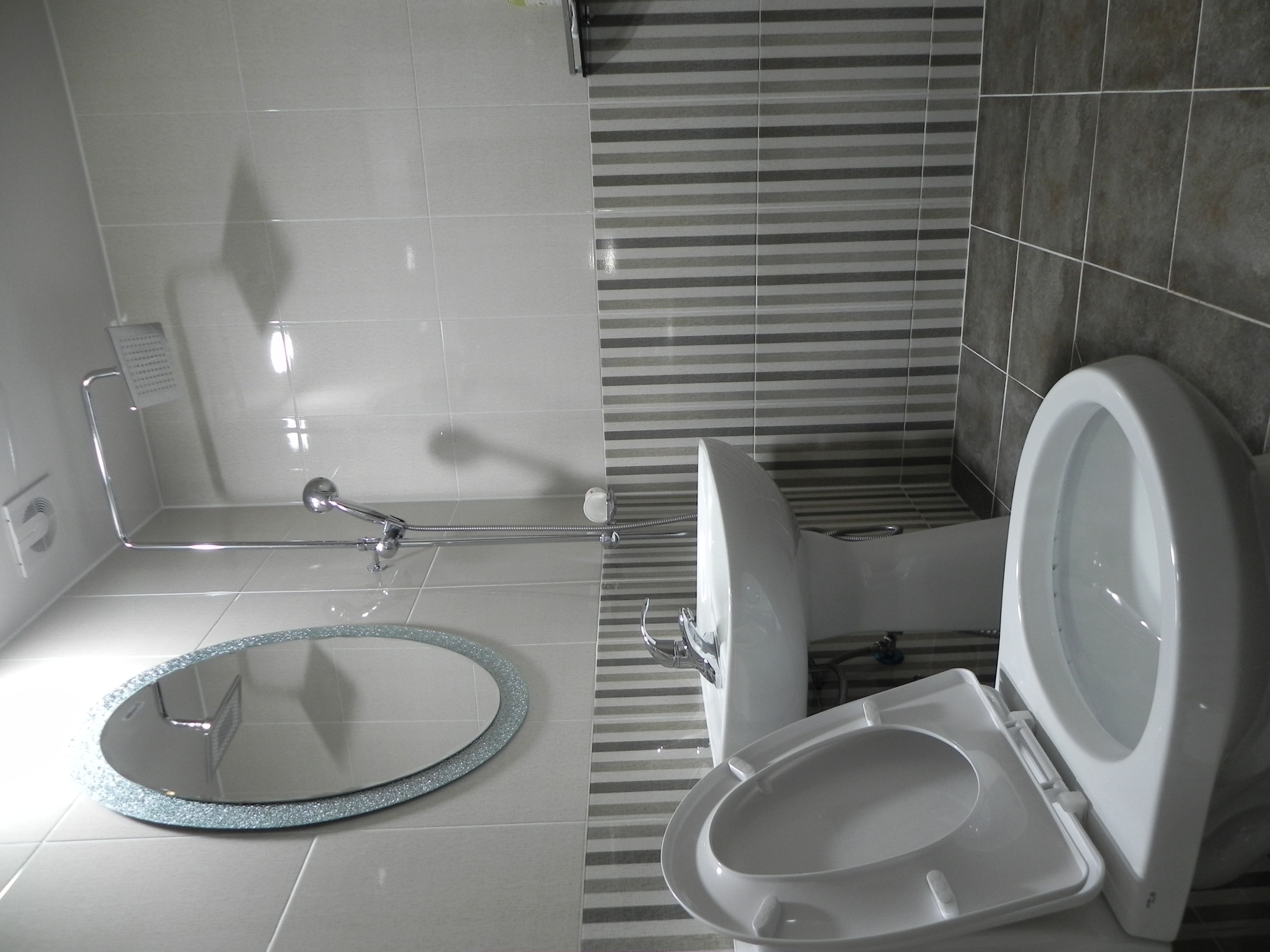 A bathroom with a shower, toilet, and a round mirror with a glittery frame.