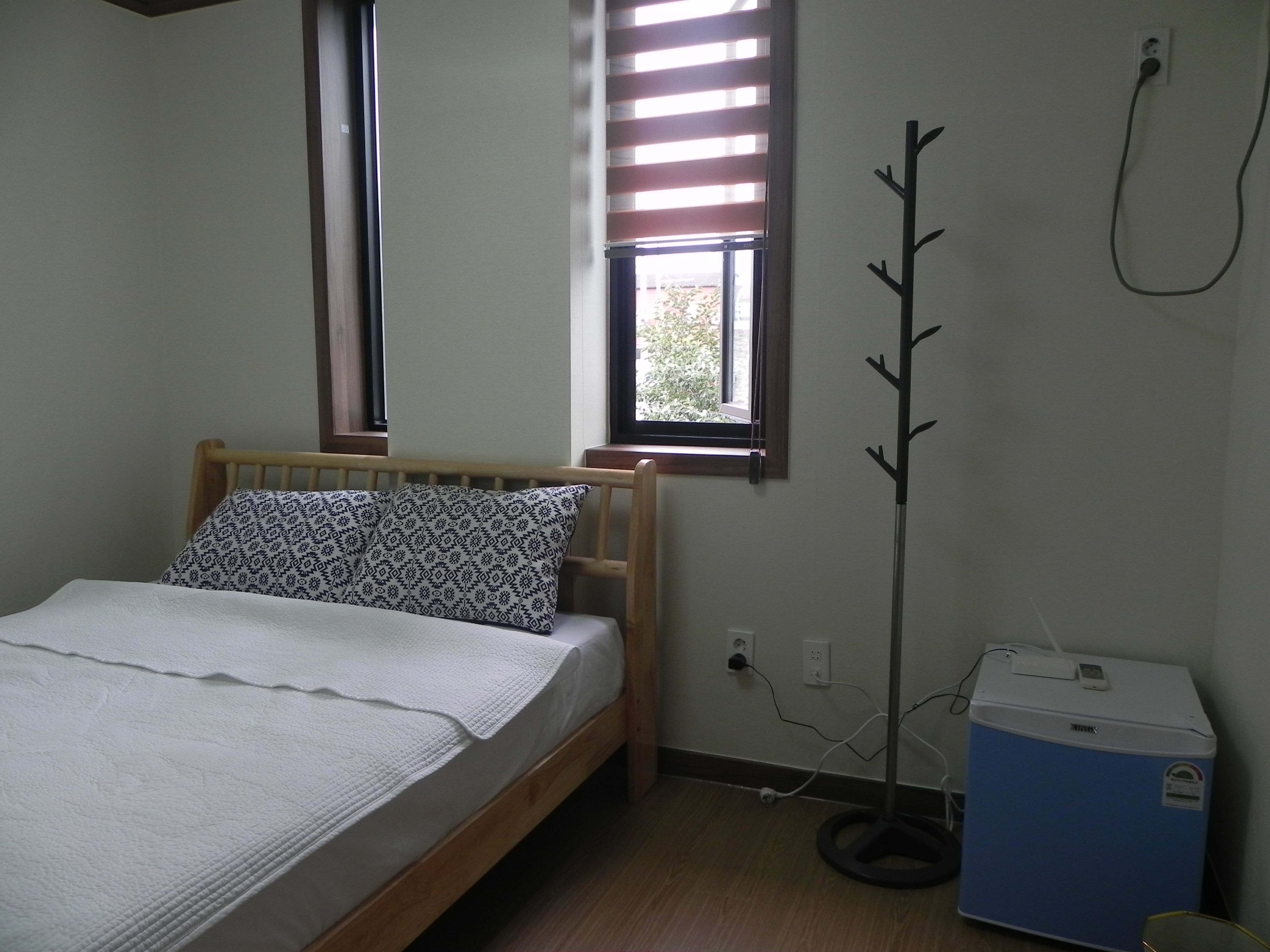 A bedroom with a bed, a window, a radiator, and a small blue appliance.