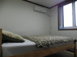 Una cama individual con ropa de cama estampada, una ventana con vistas y un equipo de aire acondicionado en la pared.