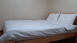 A single bed with a wooden frame and white bedding in a room with plain walls.