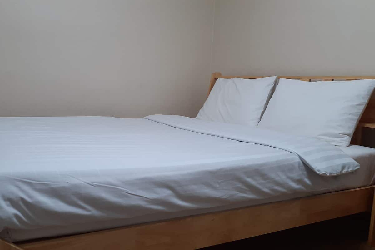 A single bed with a wooden frame and white bedding in a room with plain walls.