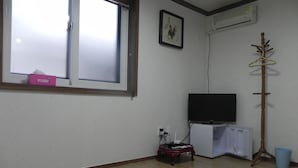 A room with a large window, a flat-screen TV on a stand, a coat rack, and a small table with a power strip.