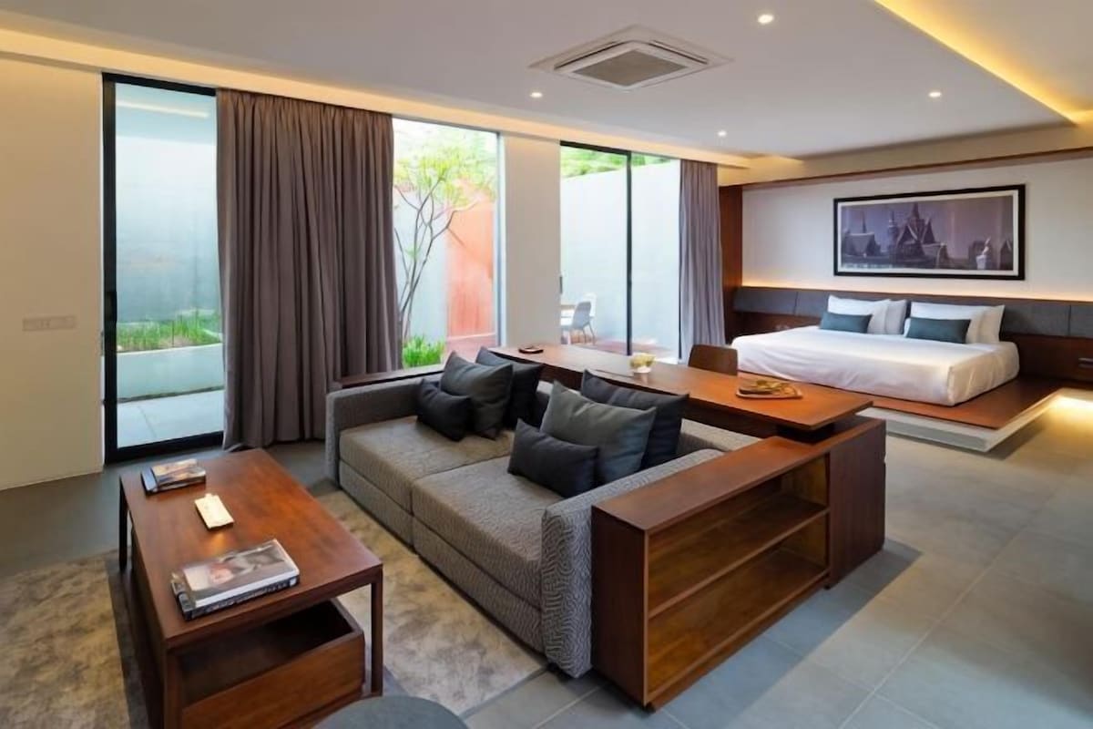 Una habitación de hotel moderna con sofá, una mesita de madera, cama y zona de comedor.