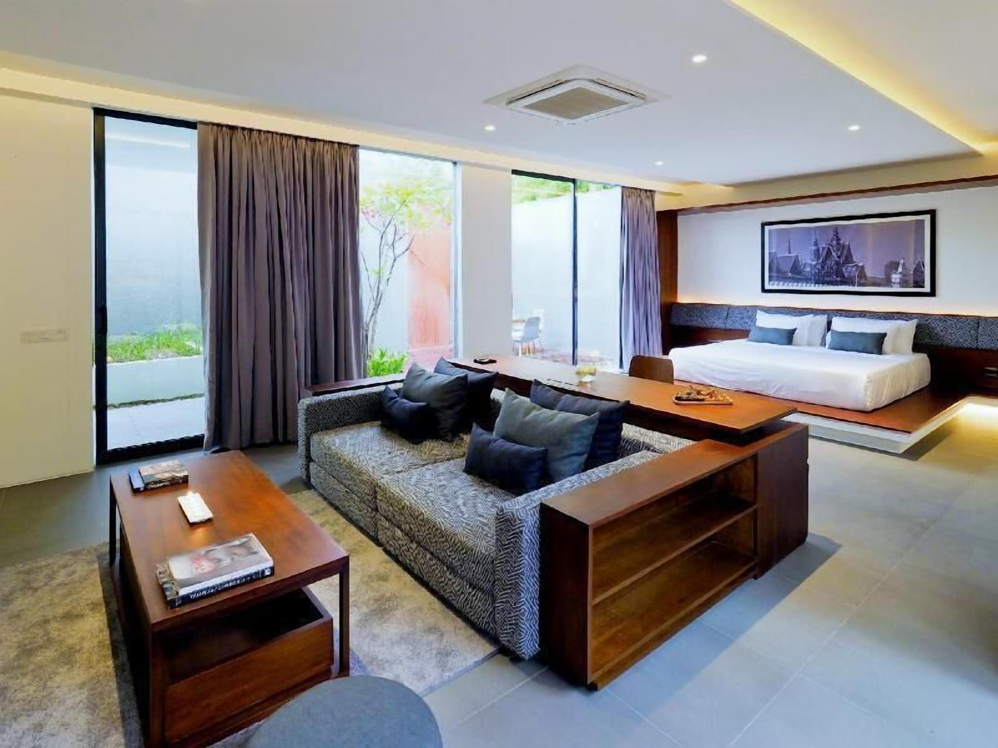 A modern hotel room with a sofa, a dining table, a bed, and large windows.