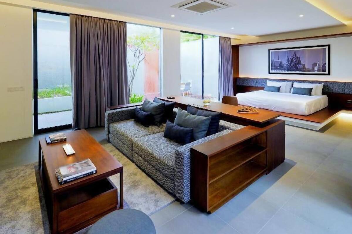 A modern hotel room with a sofa, a dining table, a bed, and large windows.