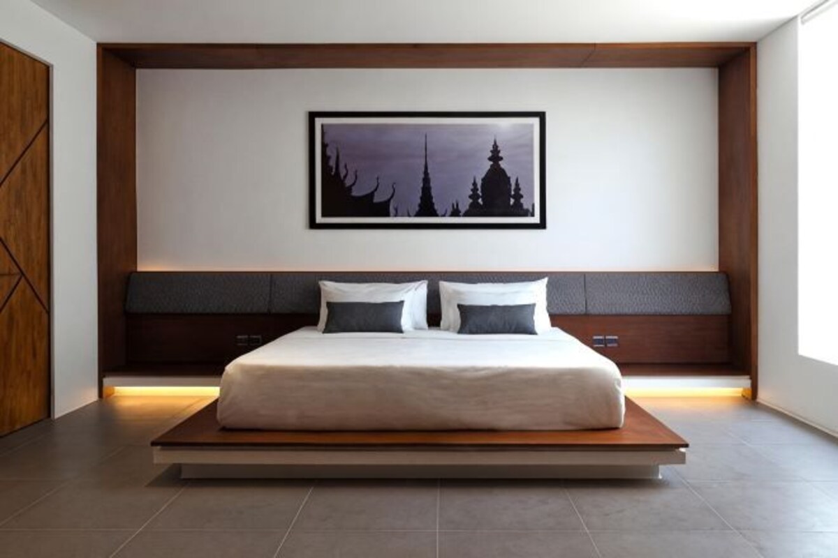 A modern bedroom with a large bed, a headboard with built-in storage, a framed picture on the wall, and a wooden floor.