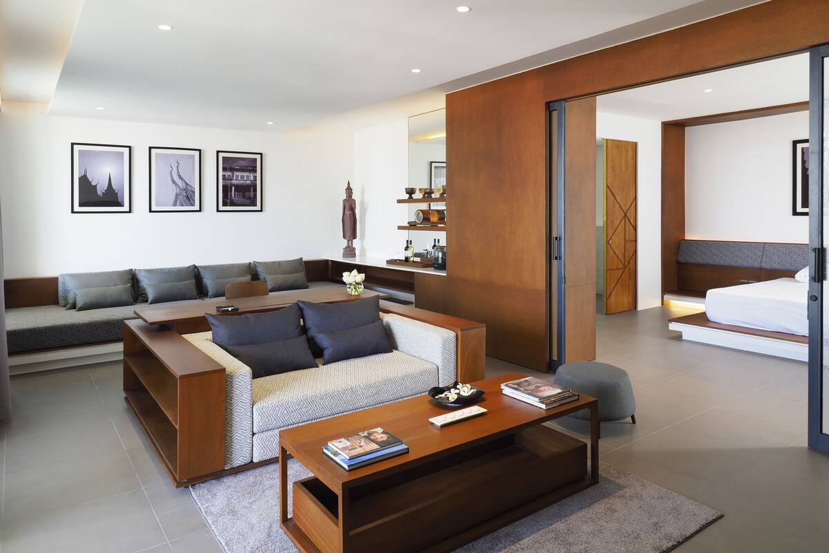 A modern living room with a sofa, coffee table, and a bed in the adjacent room.