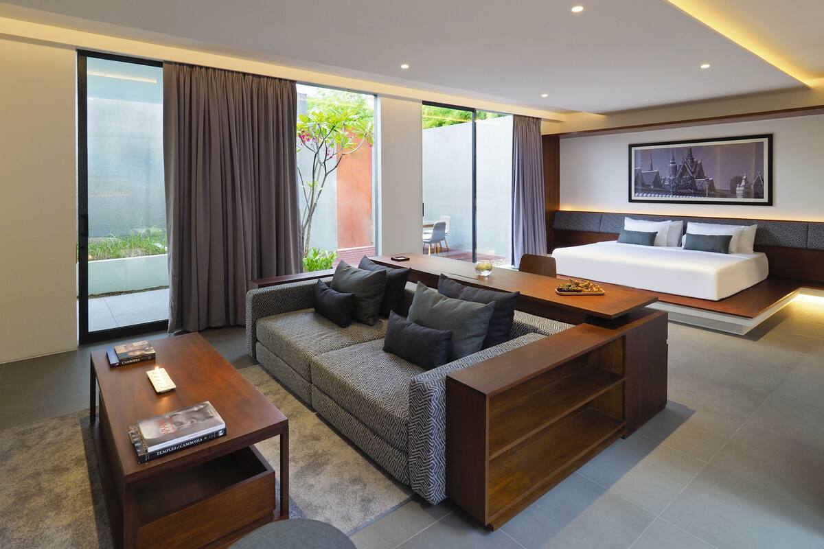 A modern hotel room with a sofa, a bed, a dining table, and a large window with curtains.