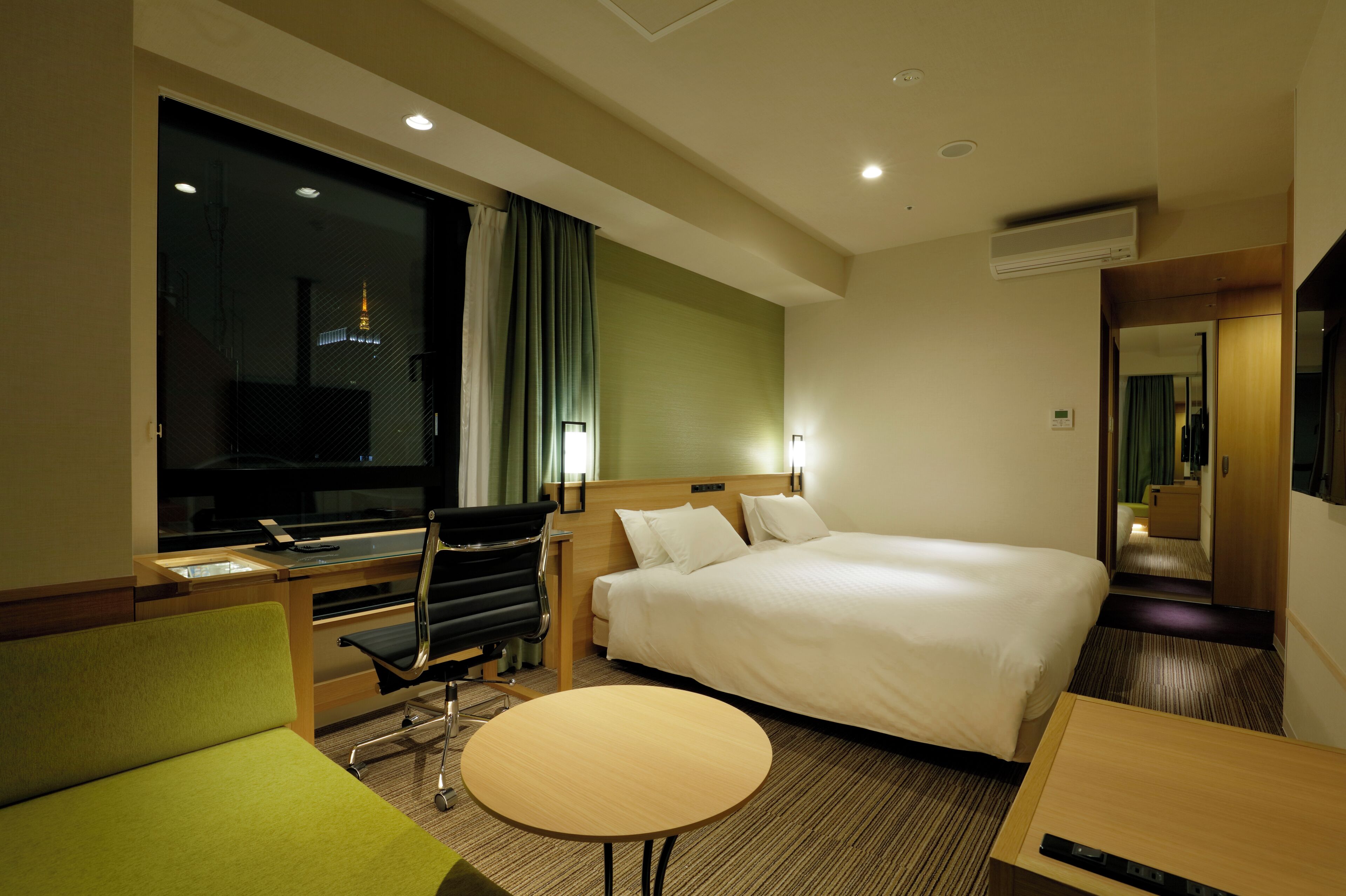 A hotel room with a bed, a desk, a chair, a round table, and a large window.
