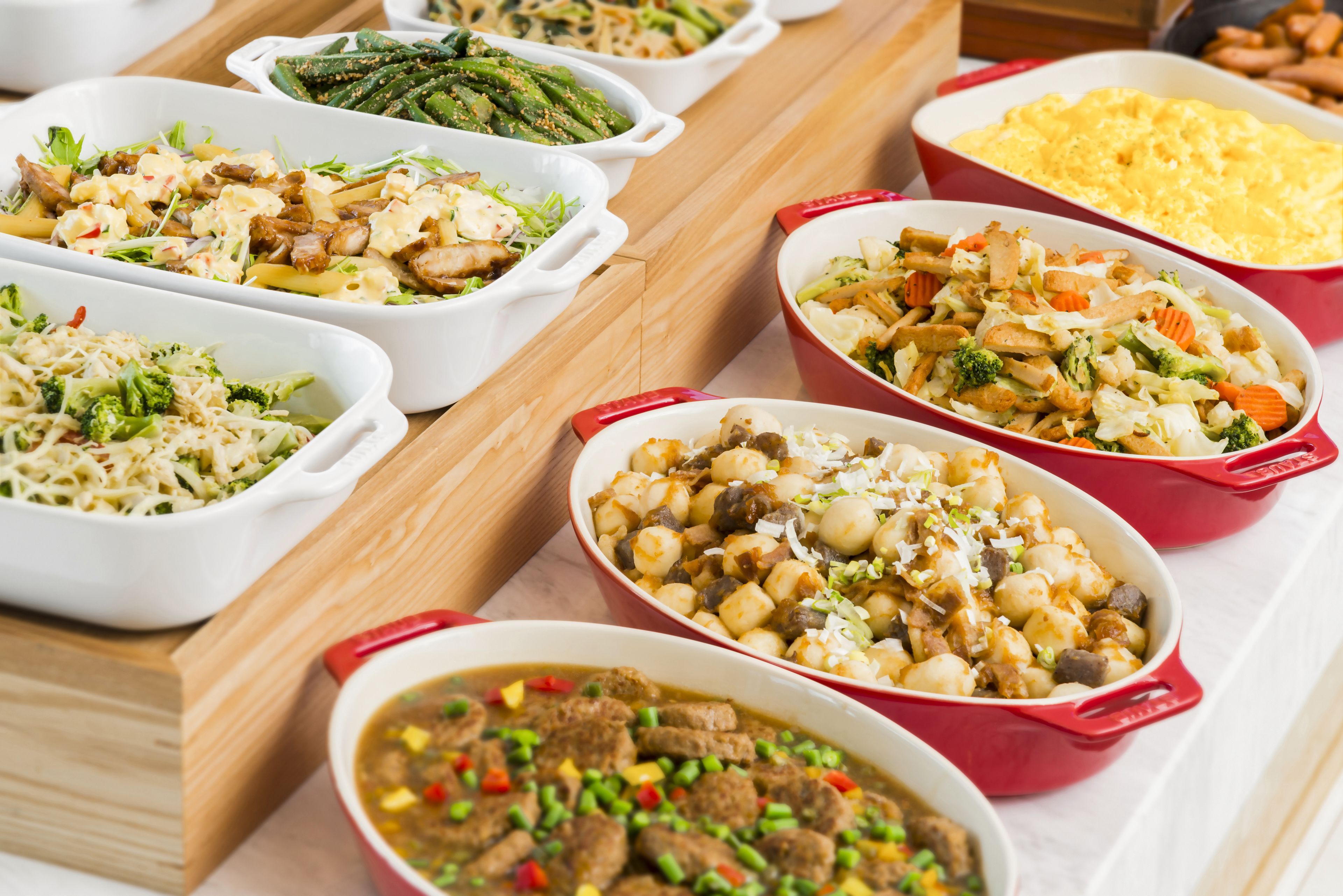 A buffet with various dishes in white and red serving dishes.