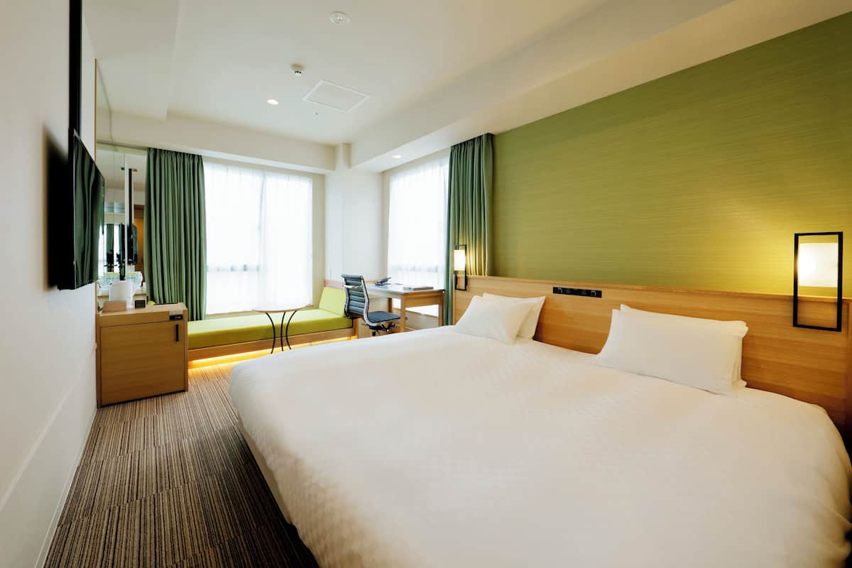 A hotel room with a large bed, a desk, a chair, a small table, a lamp, and a television.