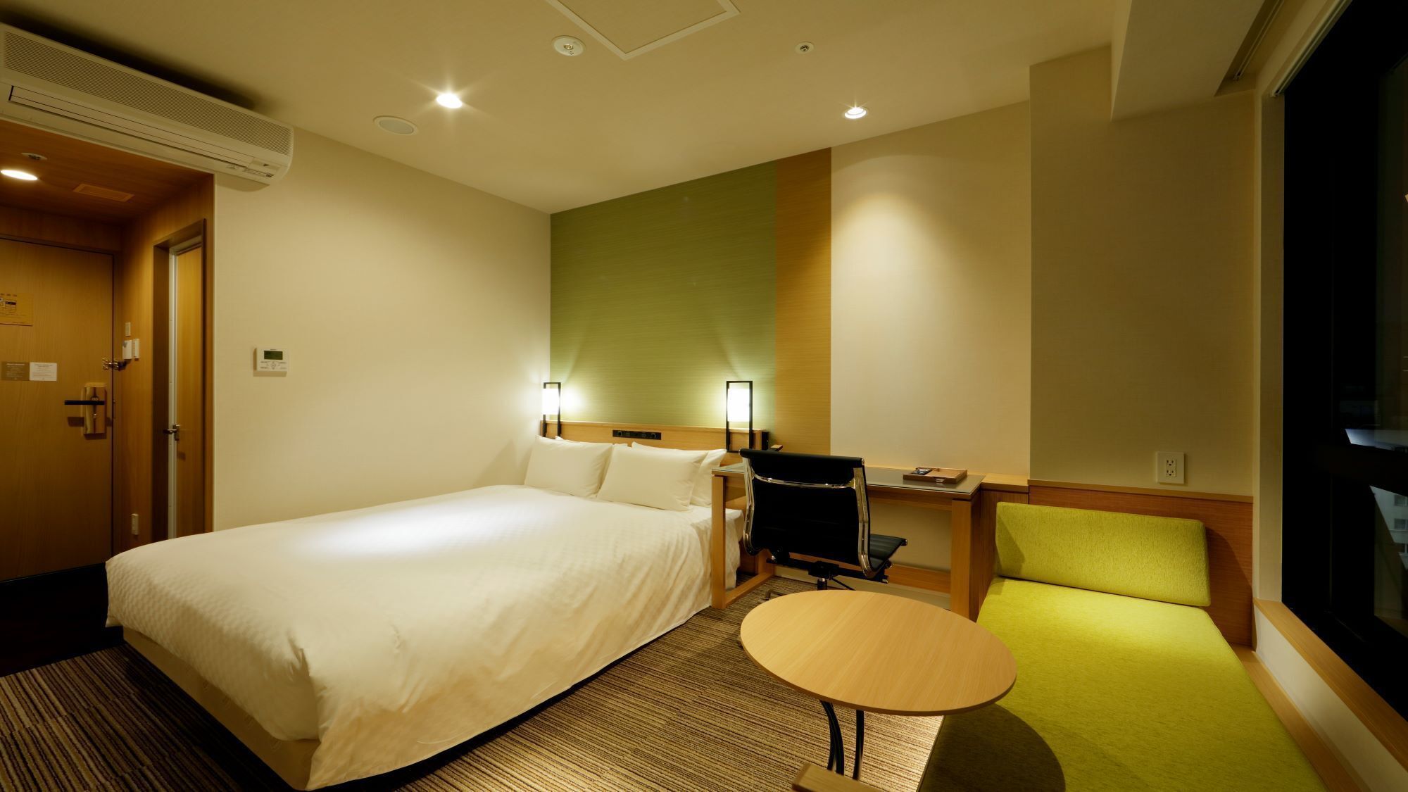 A hotel room with a large bed, a desk with a chair, a small table, and a TV.