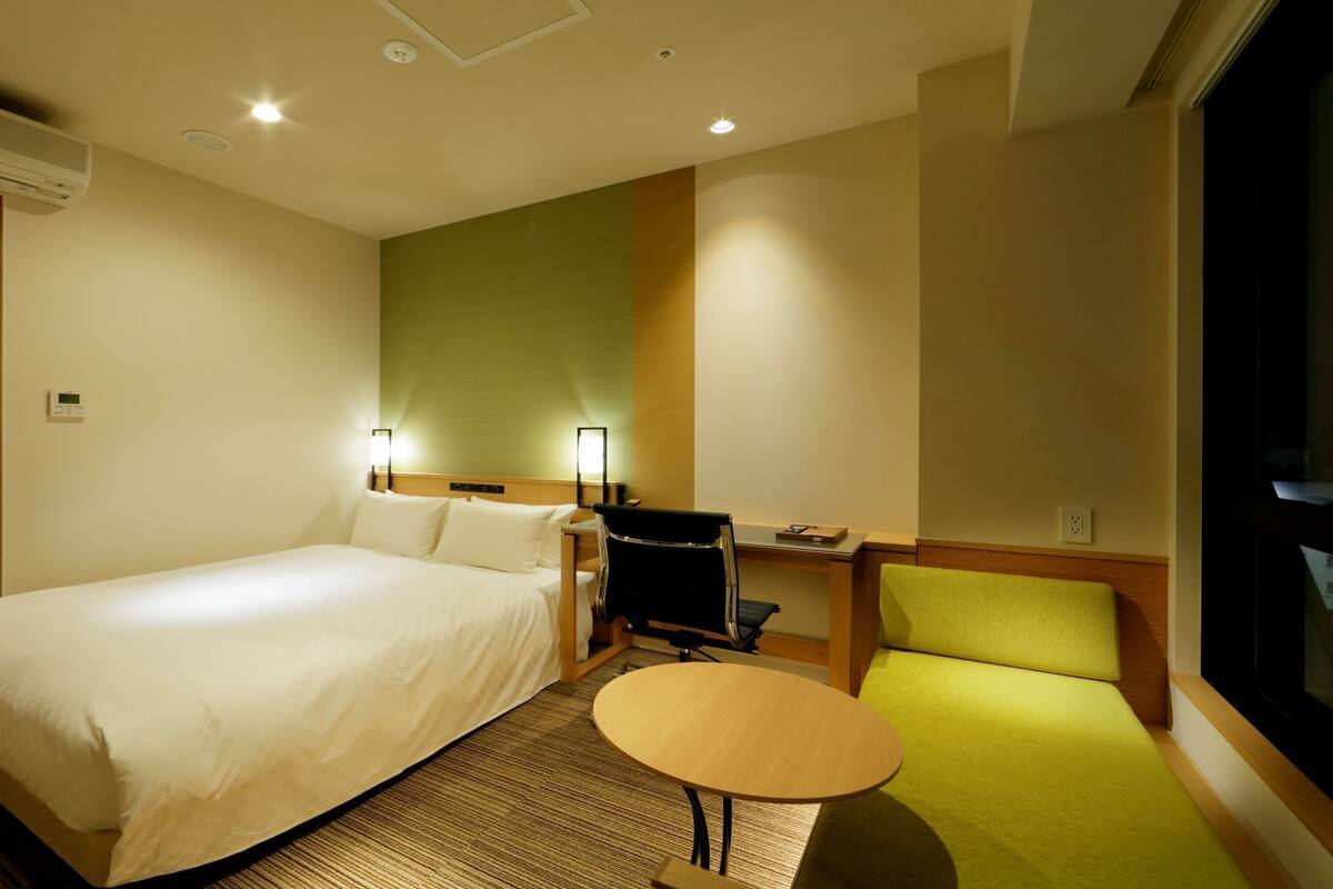 A hotel room with a large bed, a desk with a chair, a small table, and a TV.