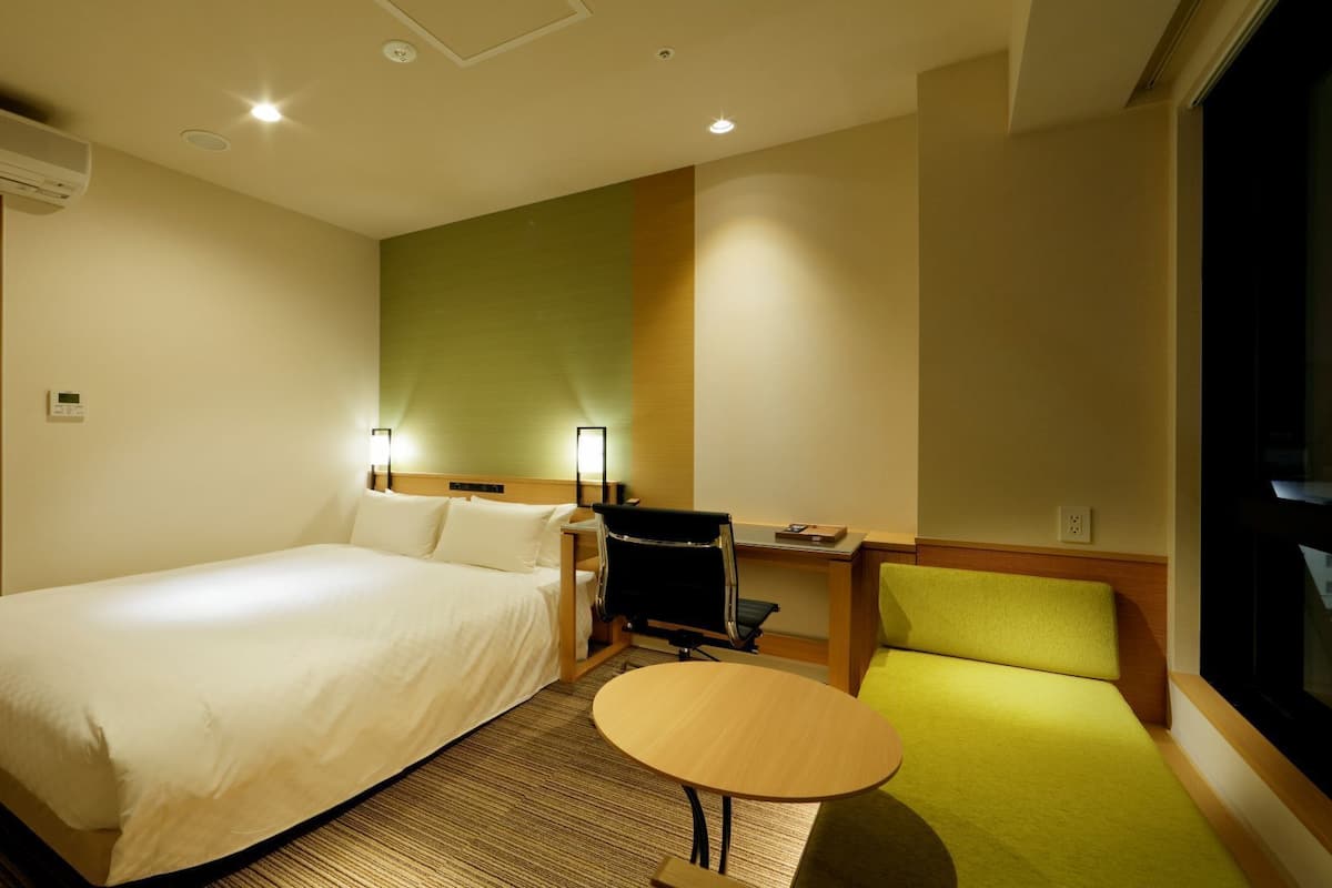 A hotel room with a large bed, a desk with a chair, a small table, and a TV.