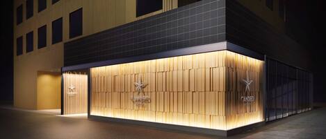 A hotel facade with a modern design, featuring a prominent logo and a well-lit entrance.