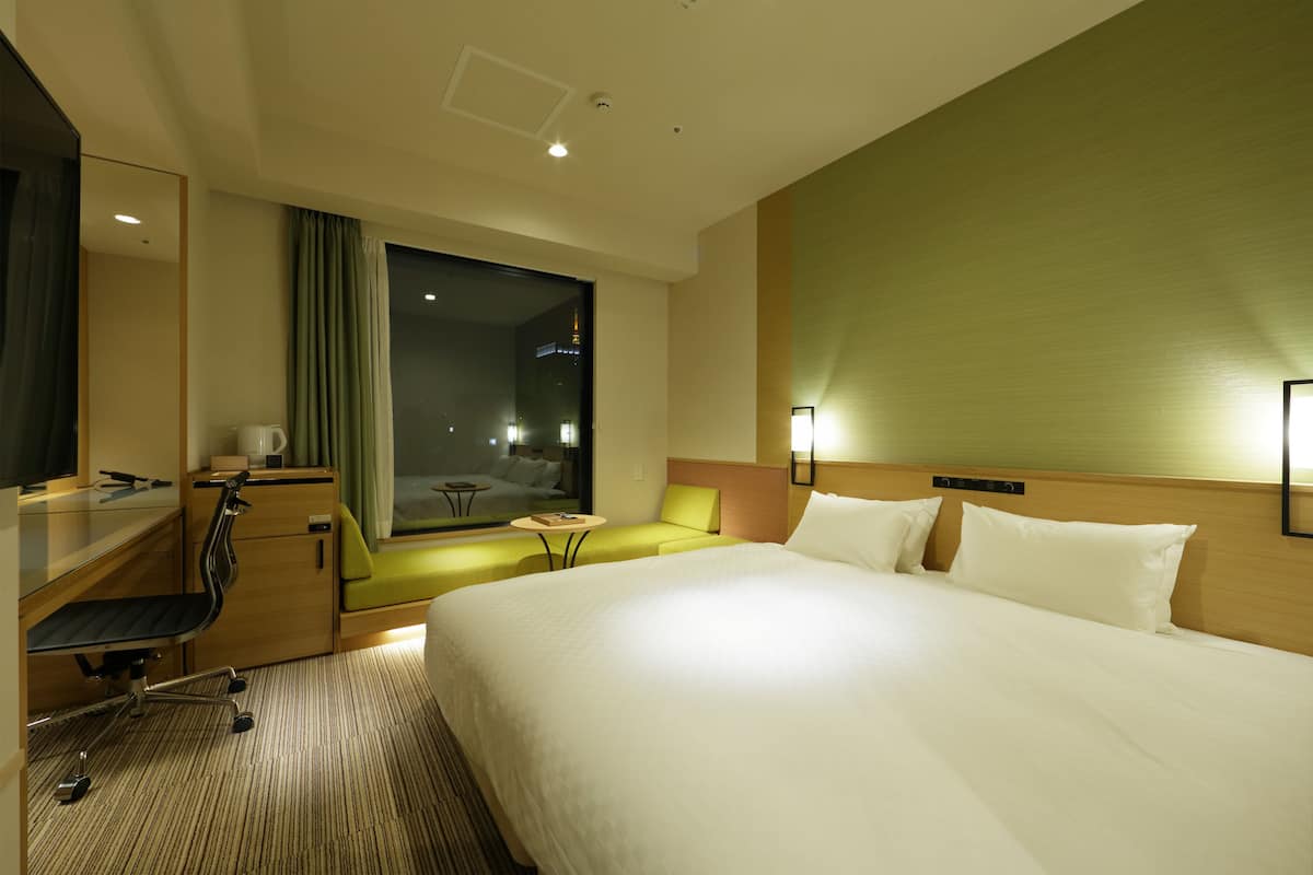 A hotel room with a large bed, a desk, a chair, a small table, and a window with curtains.