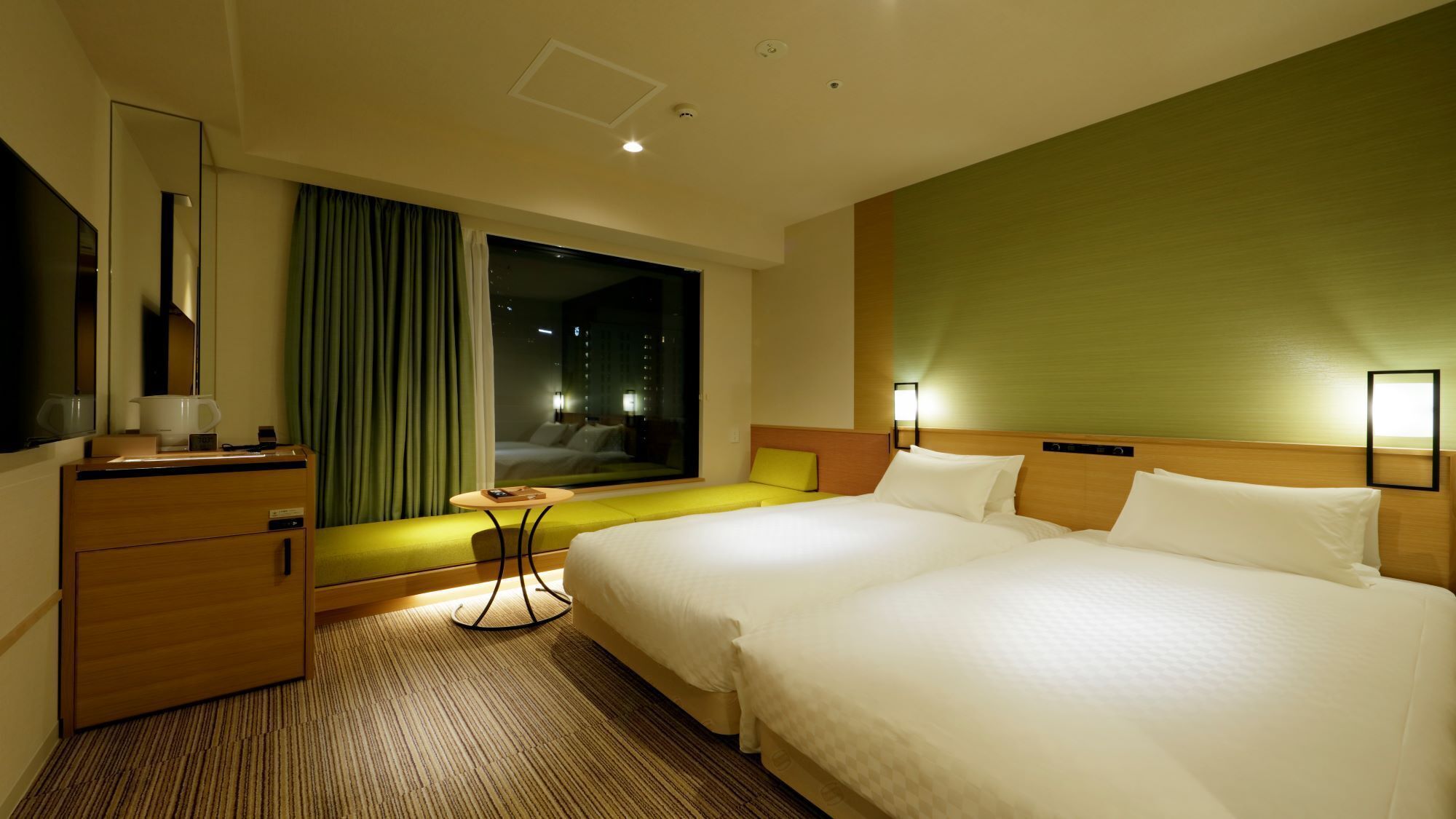 A hotel room with a large bed, a desk, a chair, a window with curtains, and a green accent wall.