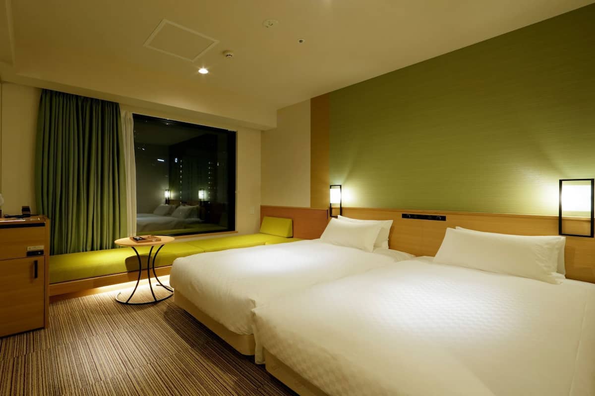A hotel room with a large bed, a desk, a chair, a window with curtains, and a green accent wall.