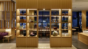 A modern interior with wooden shelving units displaying various decorative items and a central dining area with chairs and tables. - Candeo Hotels Tokyo Shimbashi (Tokyo)