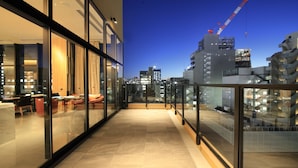 A modern hotel corridor with glass walls, a dining area with red chairs, and a view of the city skyline and construction cranes. - Candeo Hotels Tokyo Shimbashi (Tokyo)