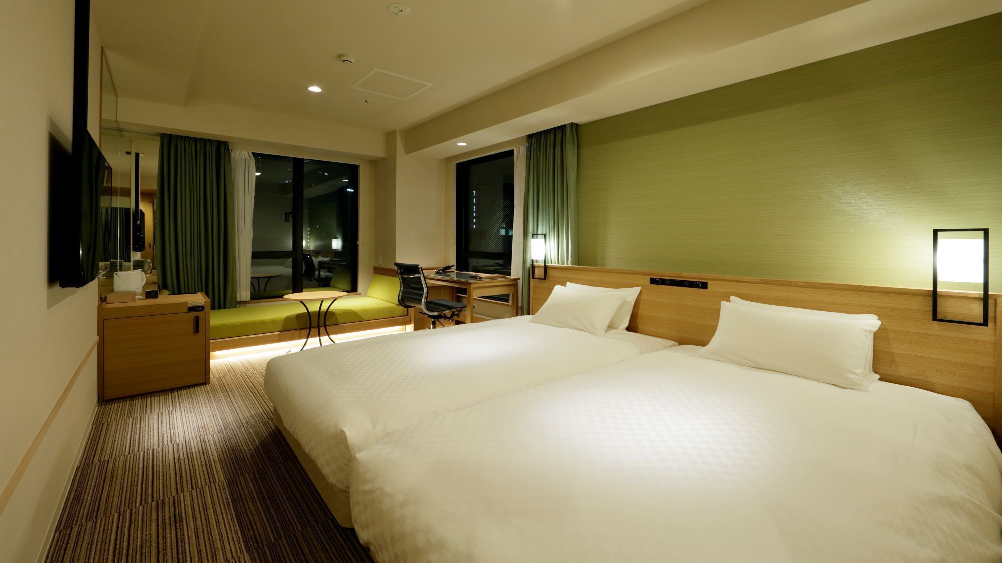 A hotel room with a large bed, a desk with a chair, a sofa, and a TV.