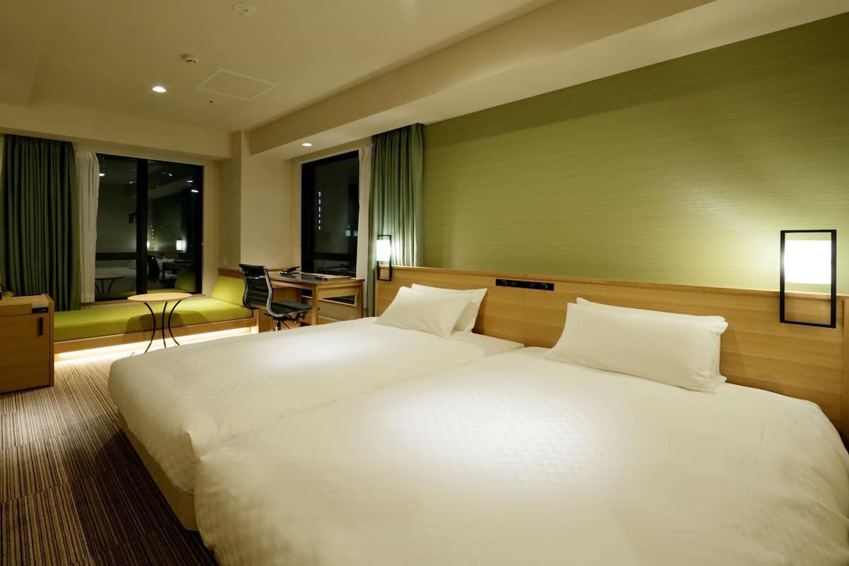 A hotel room with a large bed, a desk with a chair, a sofa, and a TV.