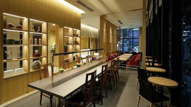 A modern dining area with a long table, chairs, and a seating area with red chairs. - Candeo Hotels Tokyo Shimbashi (Tokyo)