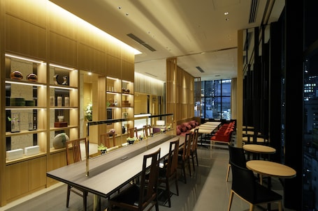 A modern dining area with a long table, chairs, and a seating area with red chairs.