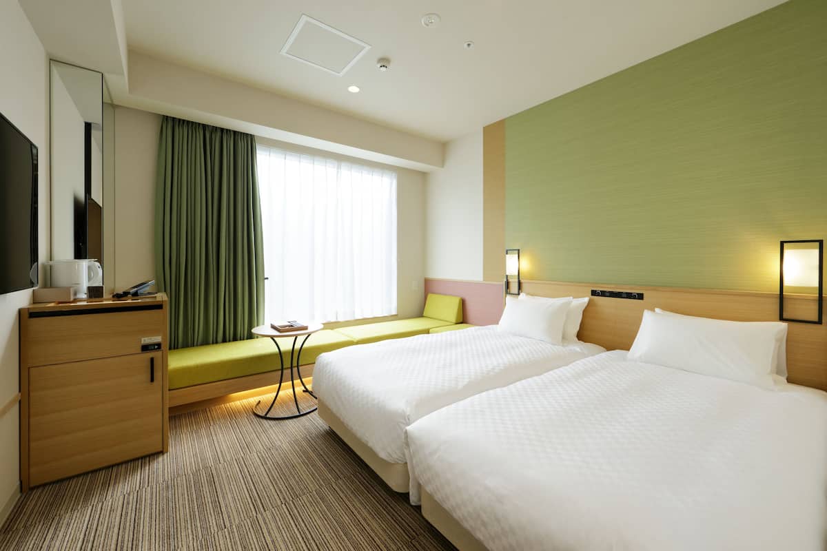 A hotel room with two beds, a desk, a chair, a small table, and a window with curtains.