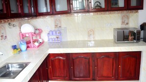 A kitchen with wooden cabinets, a sink, a microwave, and a dish rack. - Shyni Tourist Guesthouse (Hikkaduwa)